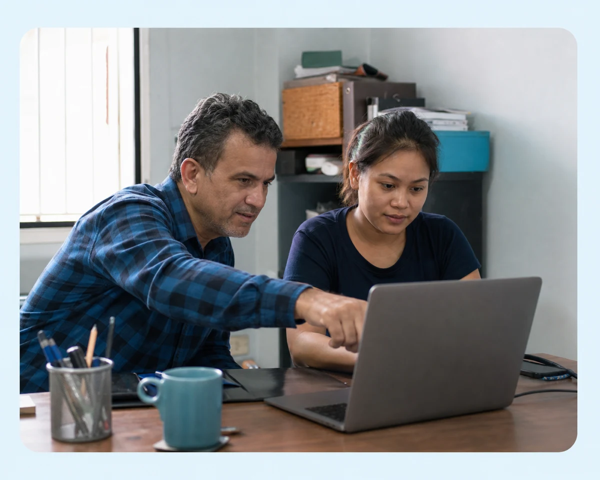 Two members of a small team working together at a laptop in a plain office.